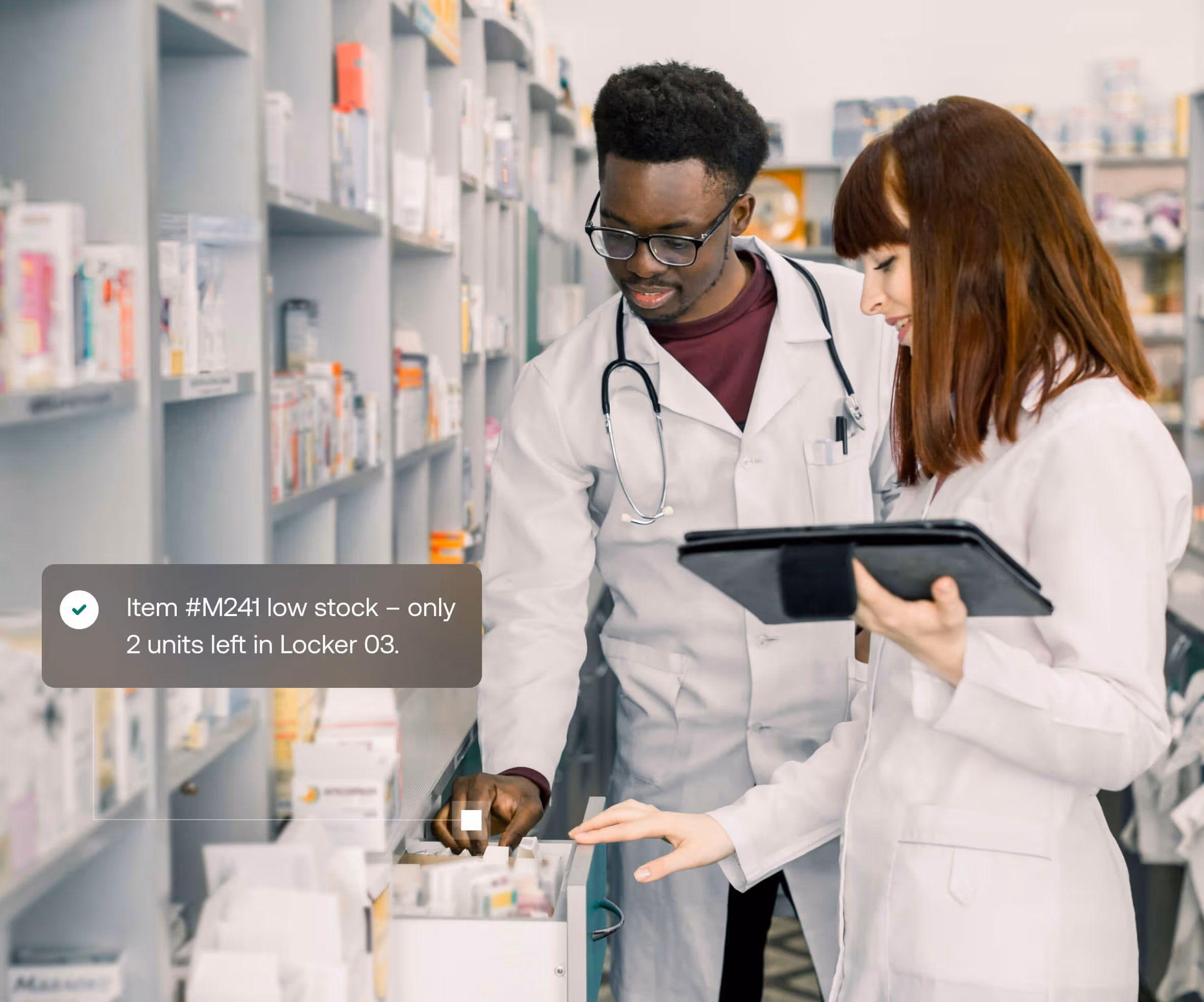 Two pharmacists in white coats checking medication stock in a pharmacy, with a notification showing low stock of item #M241, only 2 units left in Locker 03.