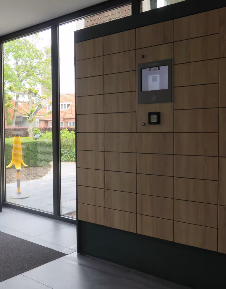 Interior view of building entrance with large glass doors, wooden panel wall with a digital display and scanner.