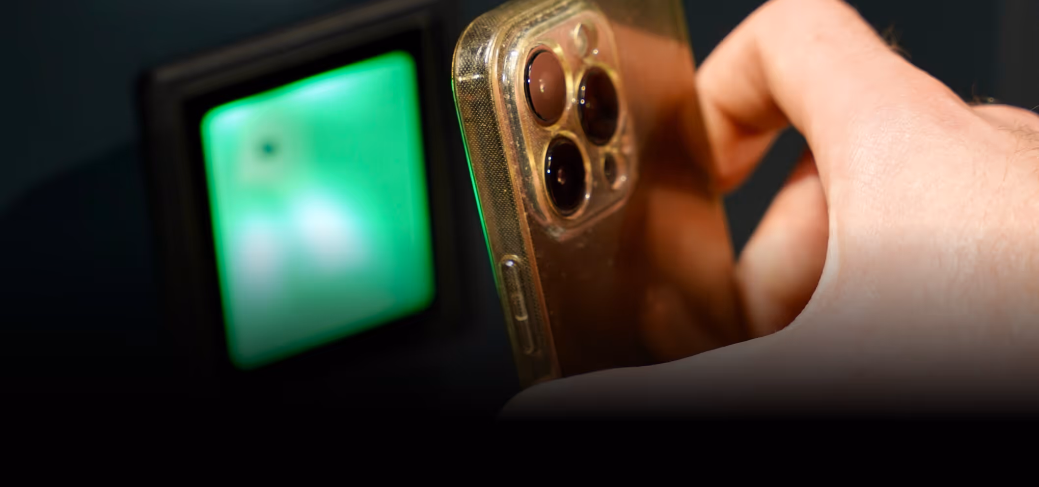 Close-up of a hand holding a smartphone with triple rear cameras near a green-lit scanner.