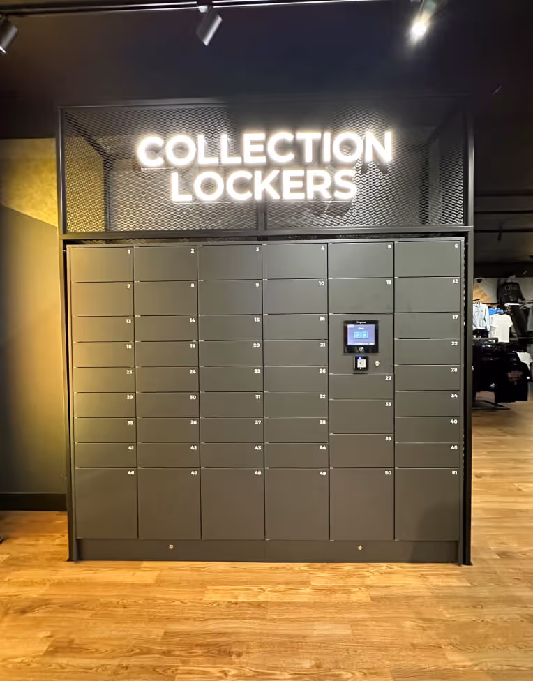 Wall of numbered grey collection lockers with a touchscreen interface in a modern indoor space with wooden floor.