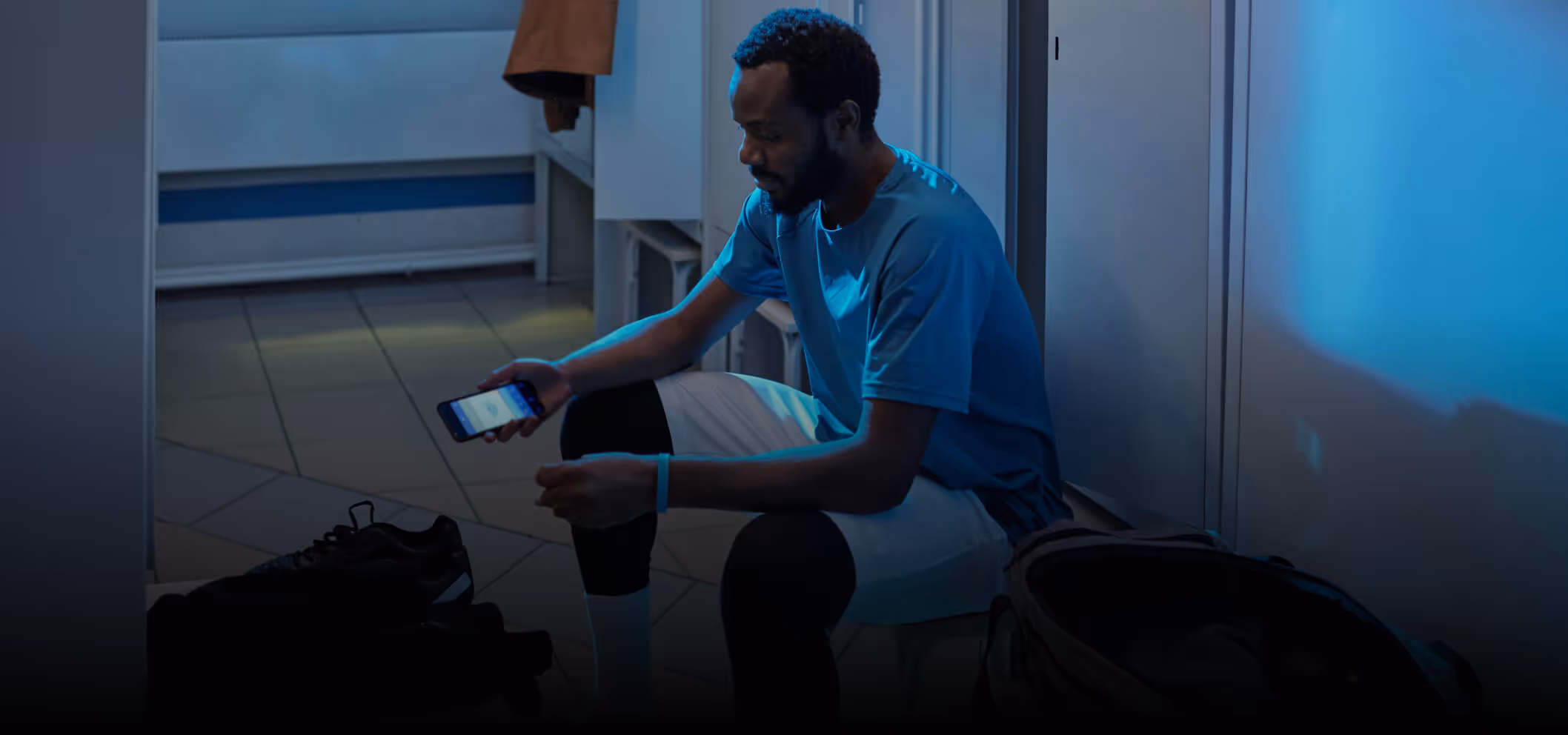 Man in sportswear sitting in a locker room looking at his smartphone.