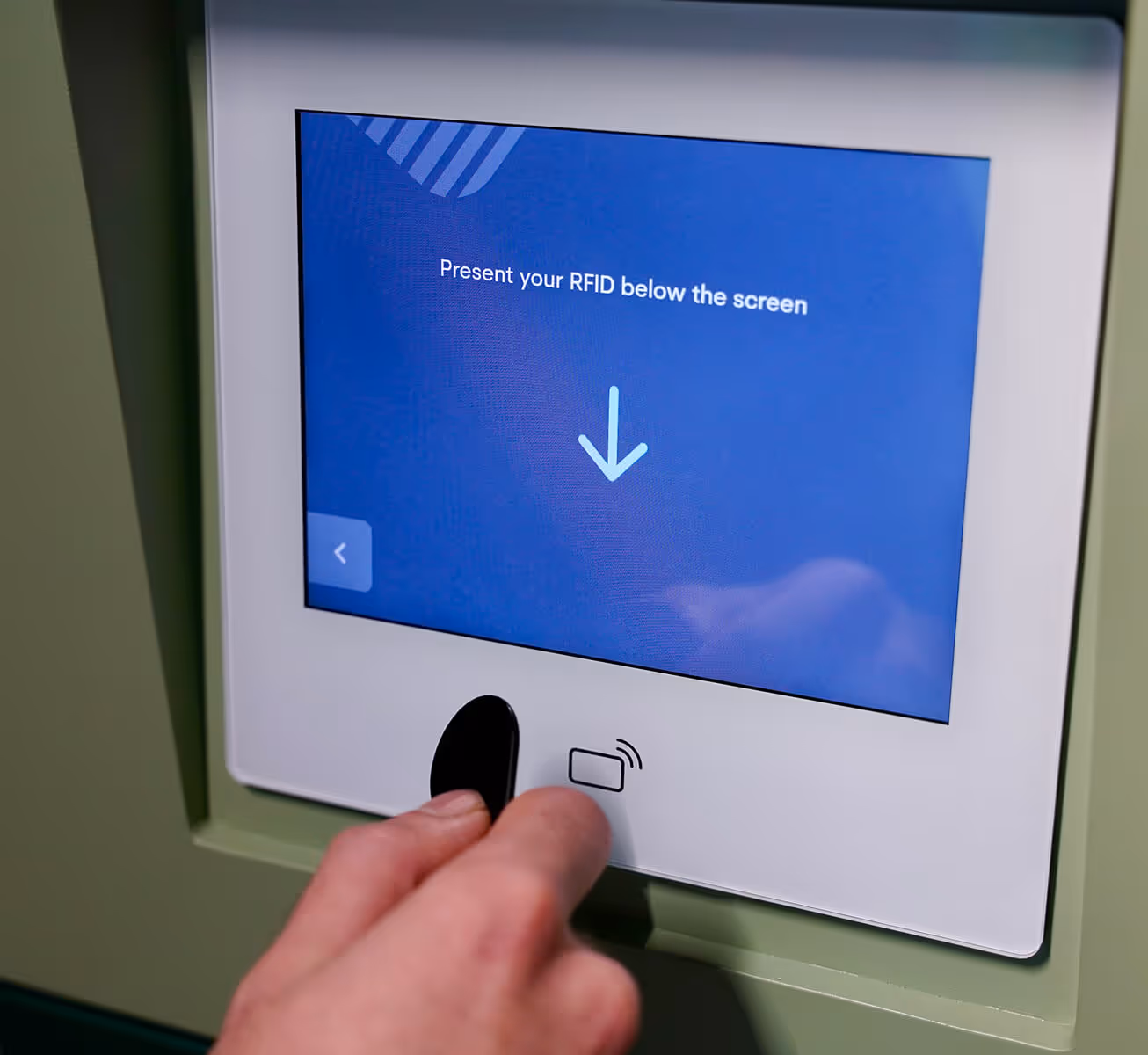 Hand holding an RFID key fob near a reader below a screen displaying 'Present your RFID below the screen' with a downward arrow.