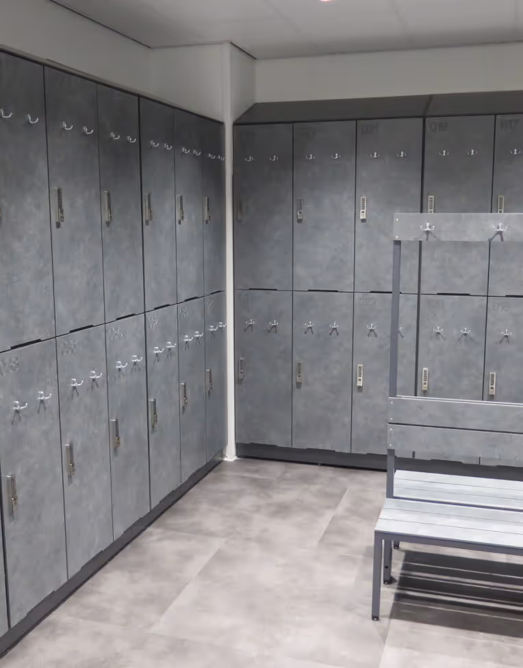 Empty locker room with gray lockers lining the walls and a wooden bench with hooks in the center.