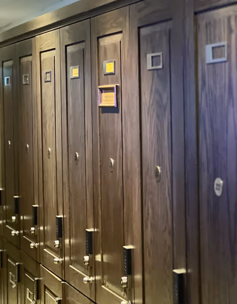Row of brown wooden lockers with combination locks and small label holders in a dimly lit hallway.