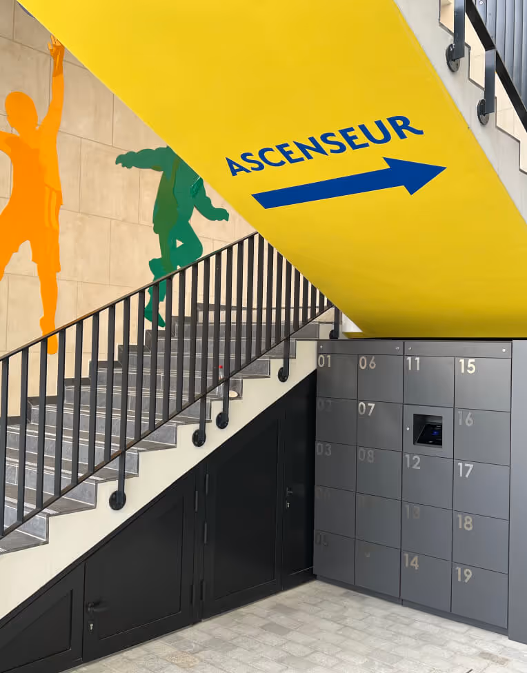 Staircase with yellow ceiling signage reading 'ASCENSEUR' and blue arrow pointing right, with colorful silhouettes of people on the wall.
