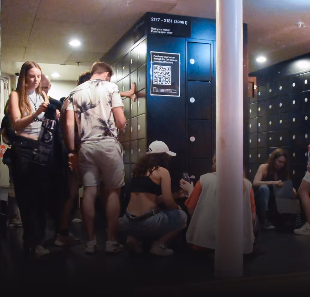 People using black lockers indoors with a QR code sign for locker purchase instructions.