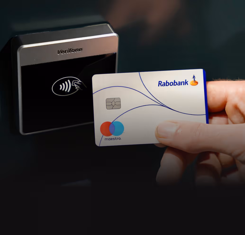 Hand holding a Rabobank Maestro card near a Verifone contactless payment terminal.