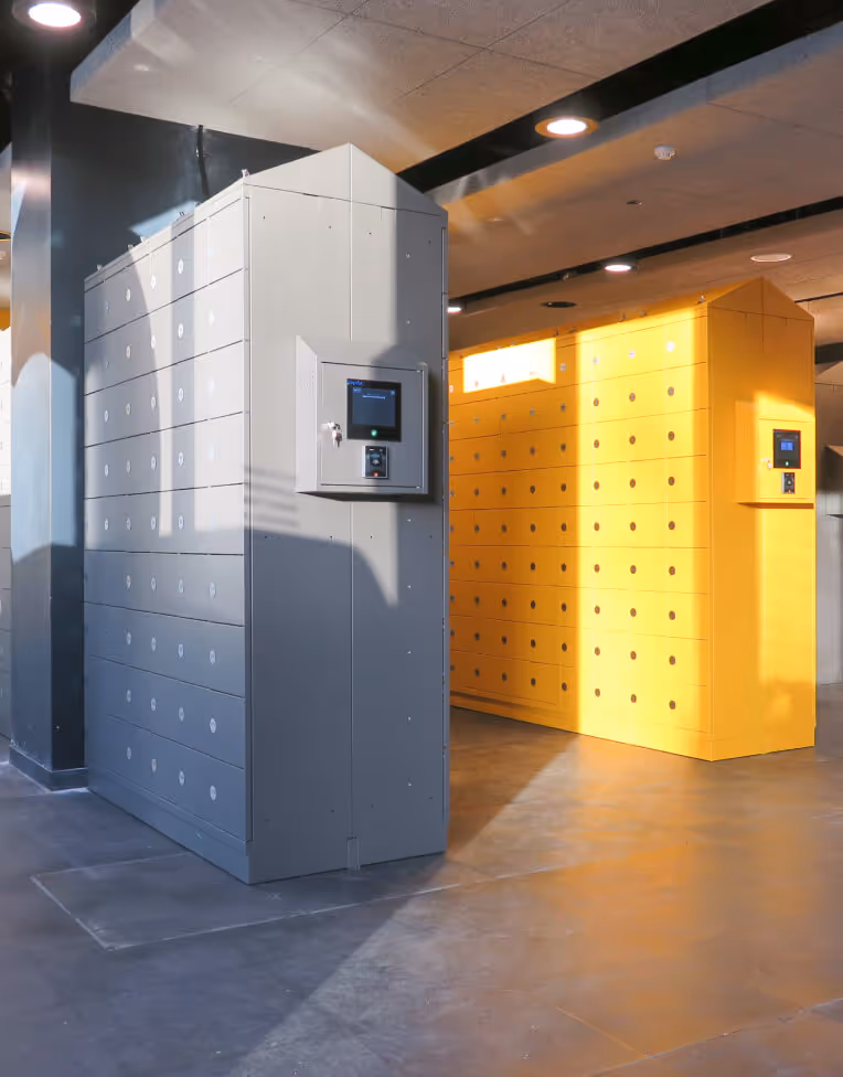 Two large parcel locker units in a modern indoor space, one grey and one yellow, each with digital screens.