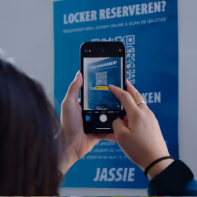Person scanning a QR code on a blue locker reservation poster with a smartphone.