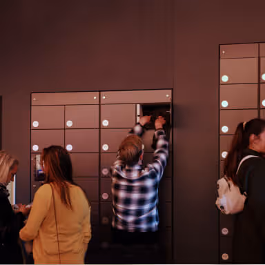 People retrieving items from a wall of parcel lockers in a public area.