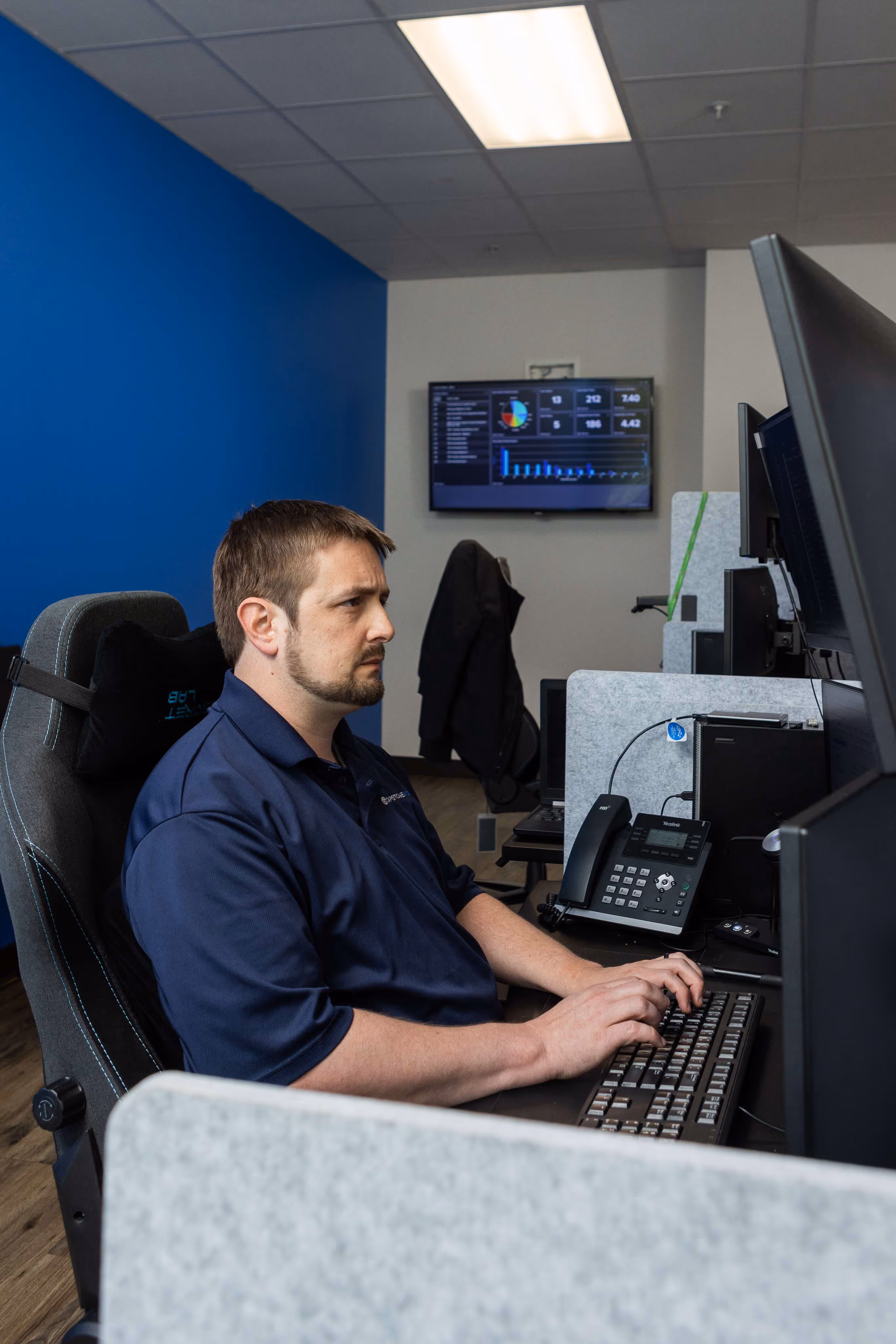 IT support technician working at multi-monitor help desk workstation with dashboard display in Austin TX office