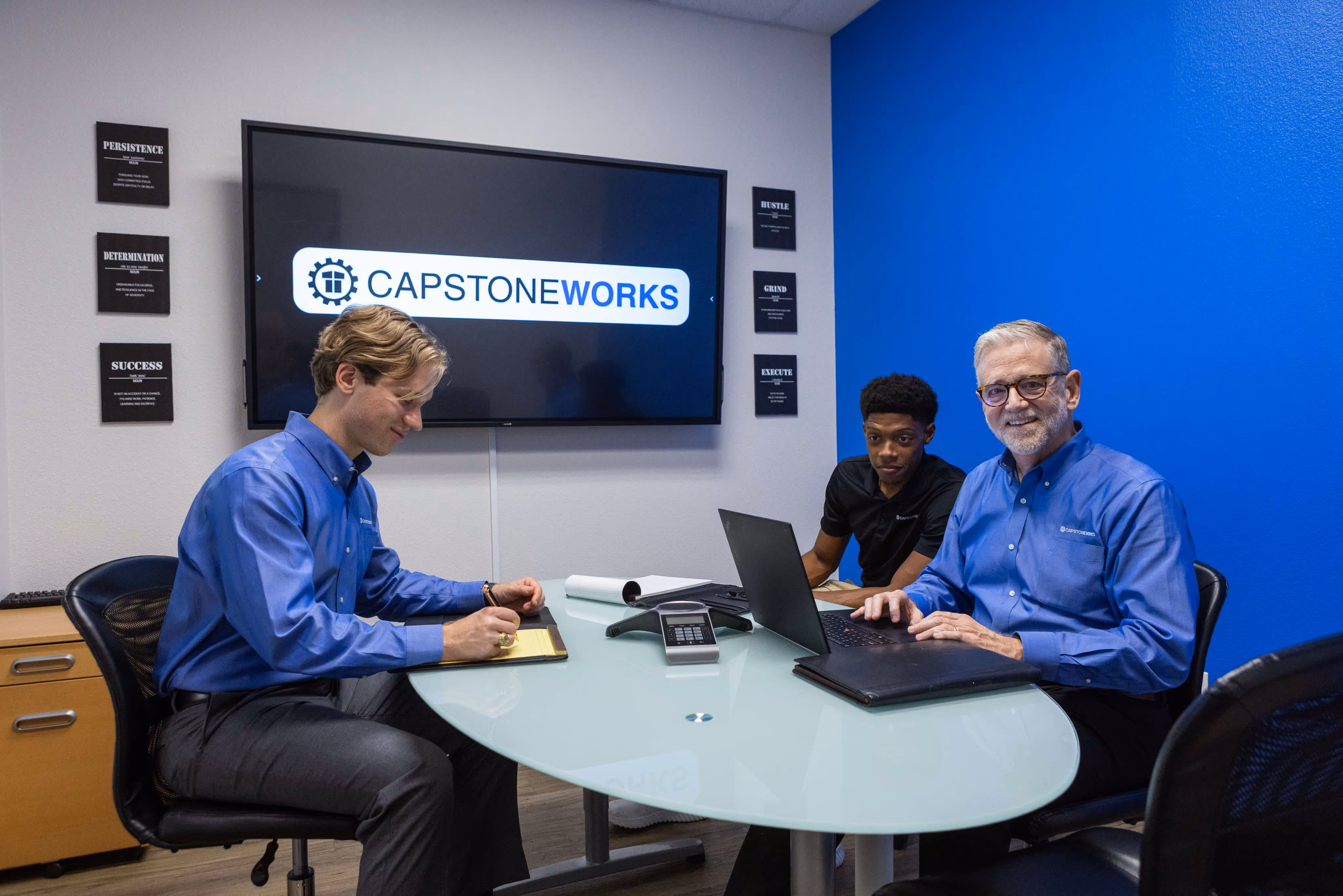 Capstone Works MSP team collaborating in conference room with IT solutions displayed on screen behind them