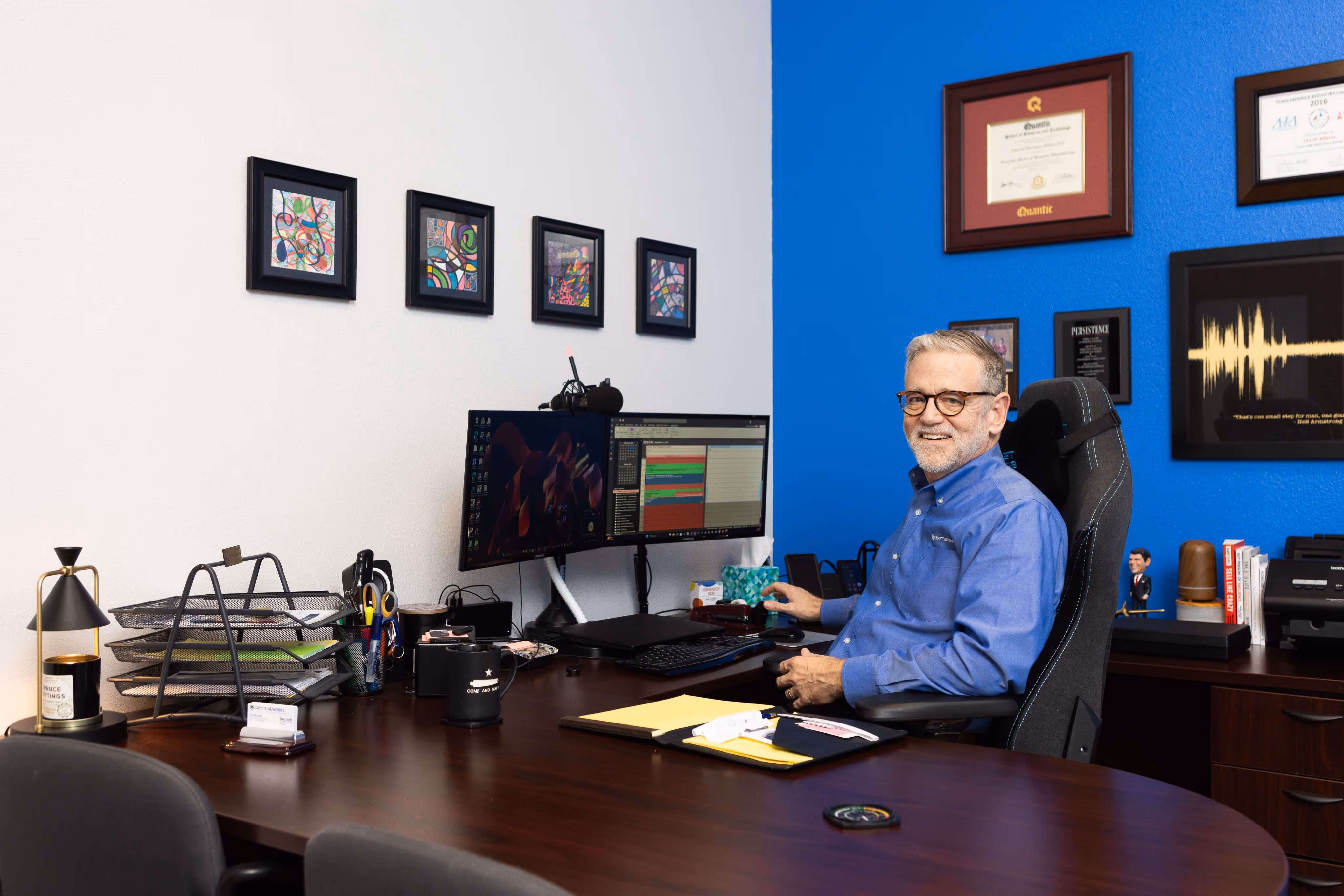 Capstone Works IT professional smiling at desk with dual monitors, diplomas, and awards in Austin TX office
