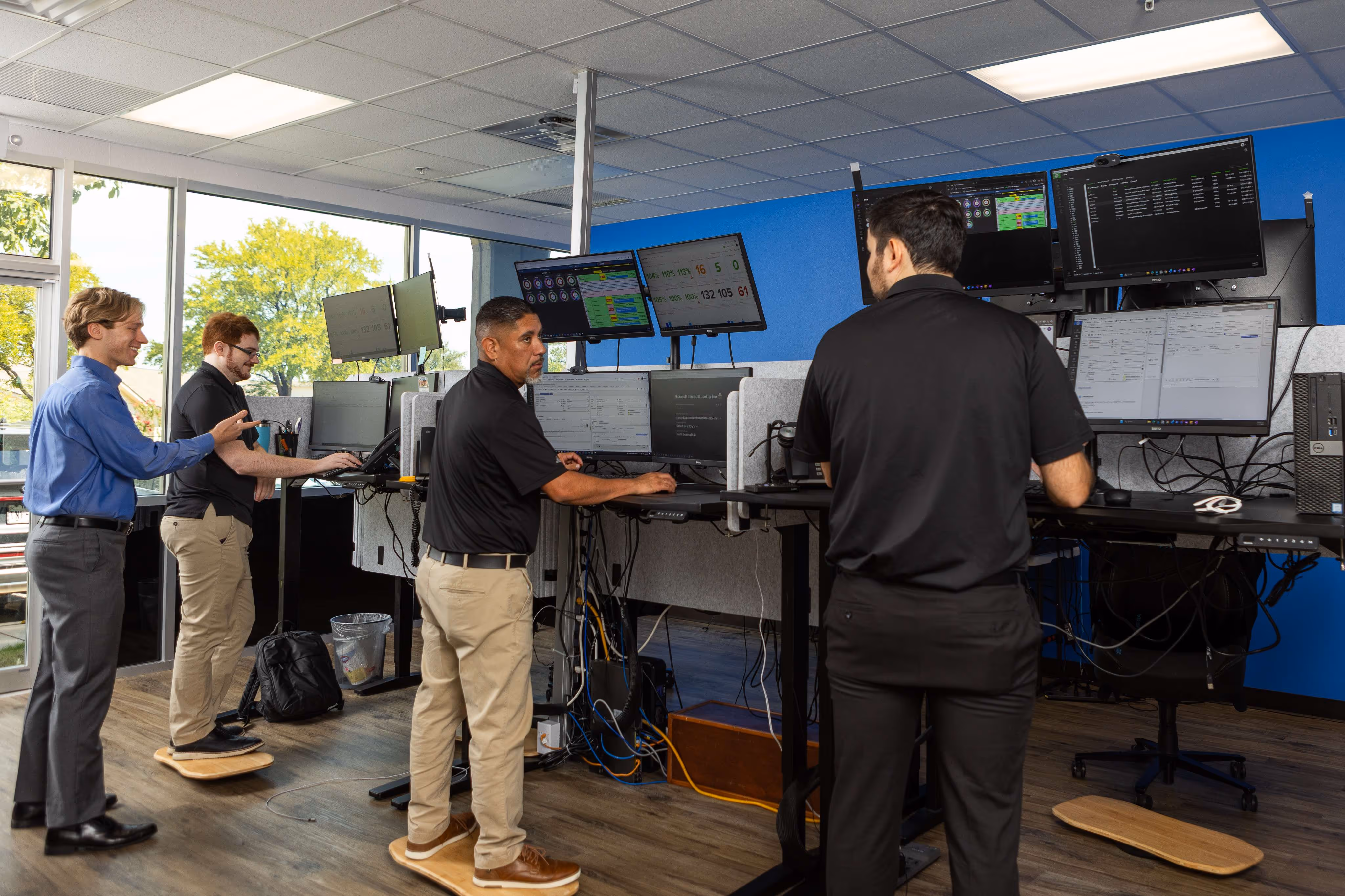 Capstone Works IT technicians collaborating at standing desks with multiple monitors in a managed services operations center