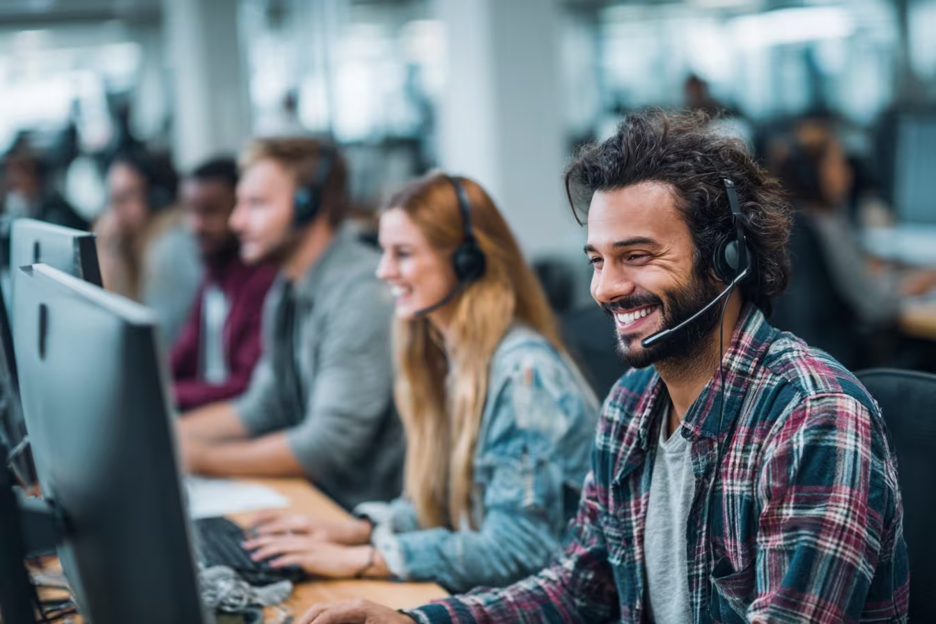 Smiling IT support technician wearing headset working at computer in busy managed services call center