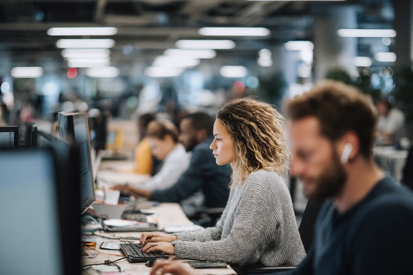 Business professionals working at computers in a modern open office, focused on IT support tasks at their workstations