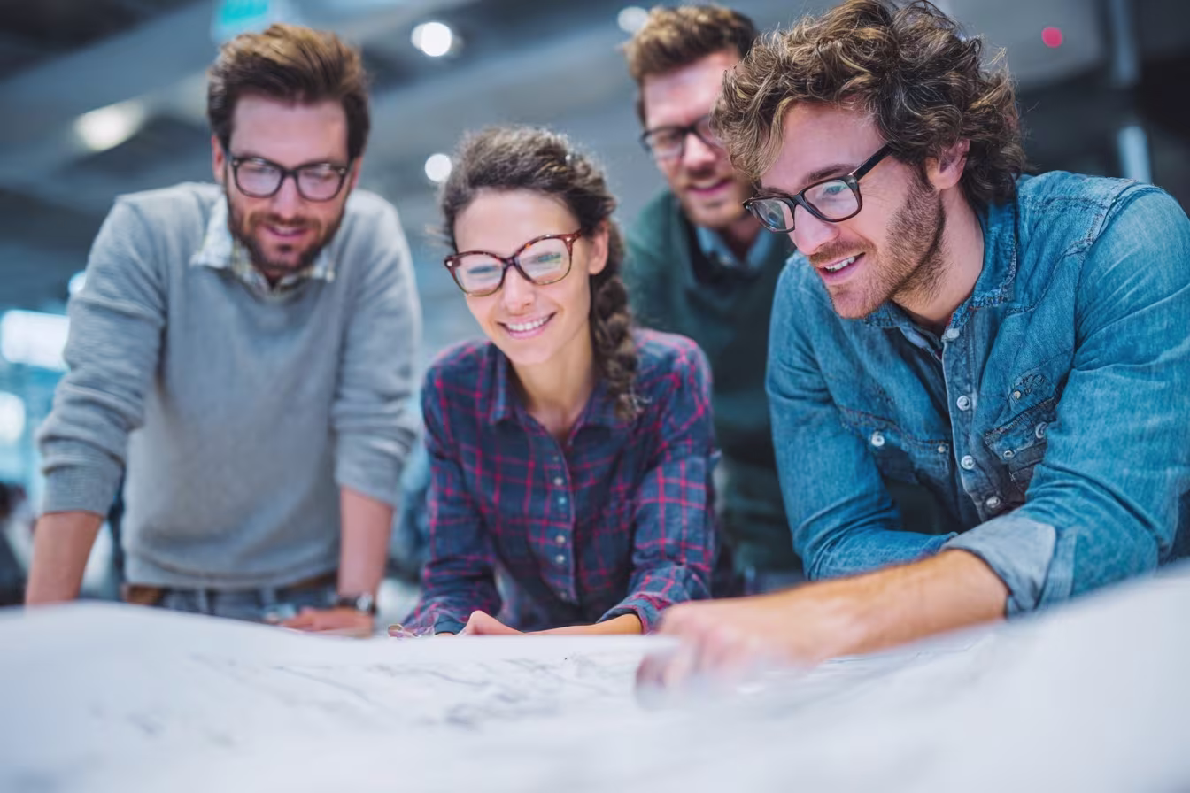 Four professionals wearing glasses reviewing IT network plans together at a table in a modern office