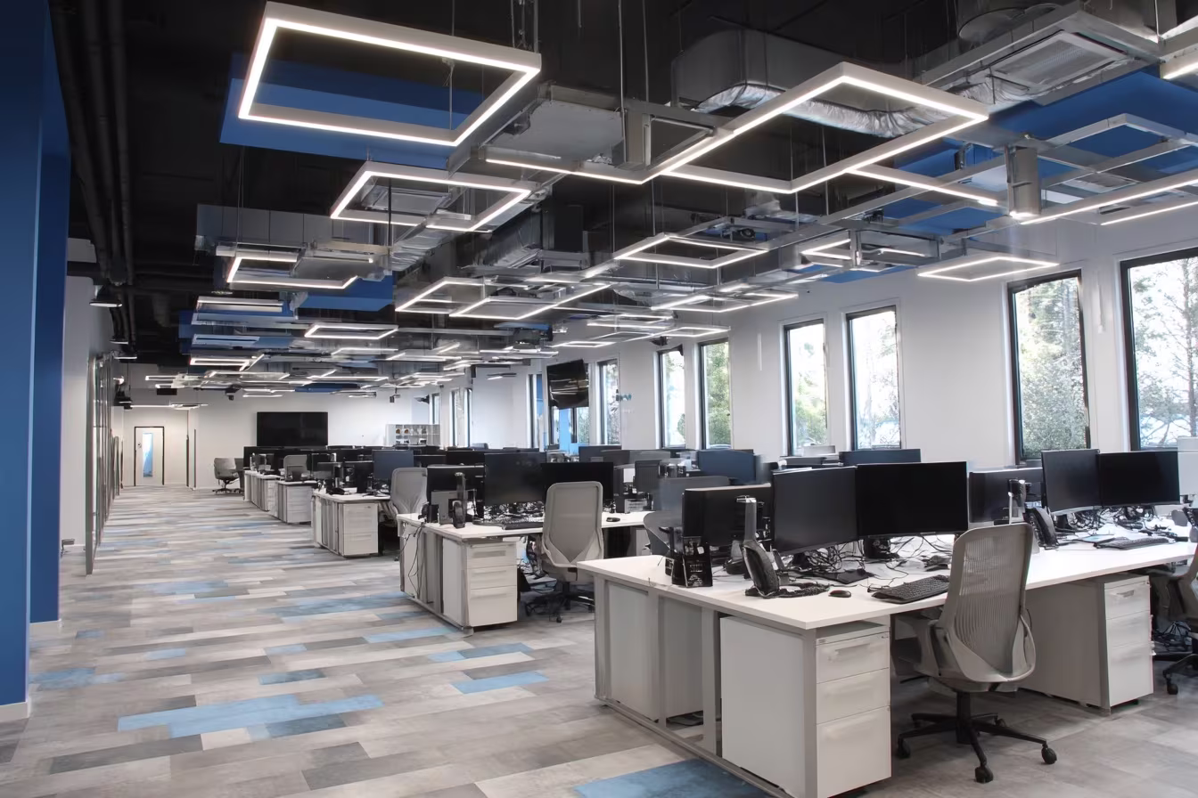 Modern open-plan IT office with workstations, dual monitors, ergonomic chairs, and geometric LED ceiling lights in Austin TX