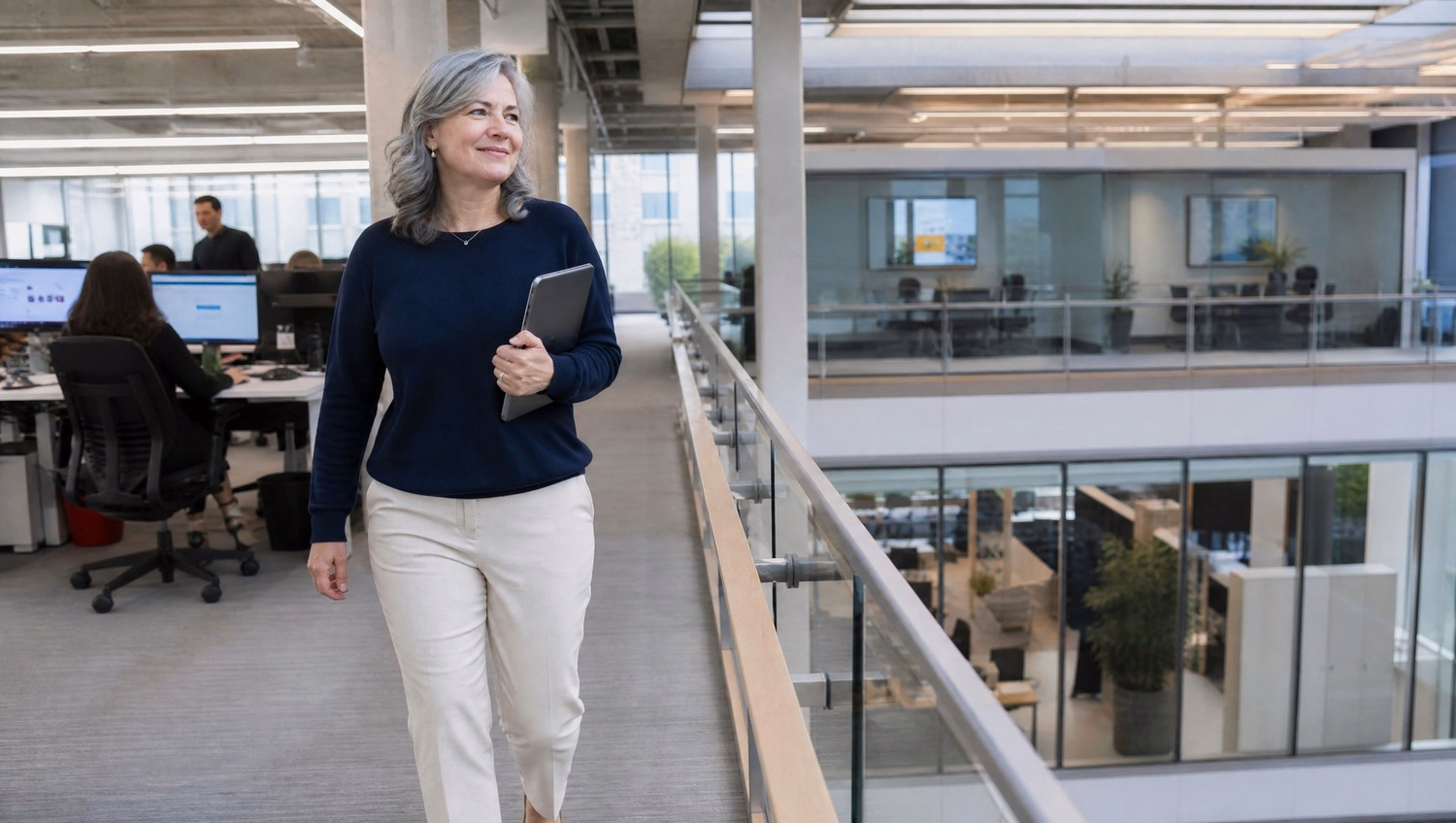Woman with tablet walks across office atrium walkway 63 chars