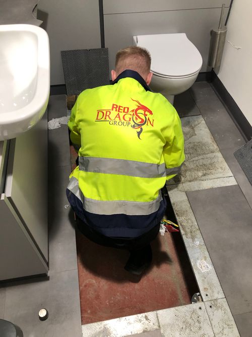 Red Dragon employee fixing something underneath the floor in a bathroom.