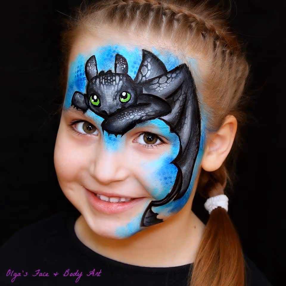 Smiling girl with a black dragon face paint with green eyes on blue background.