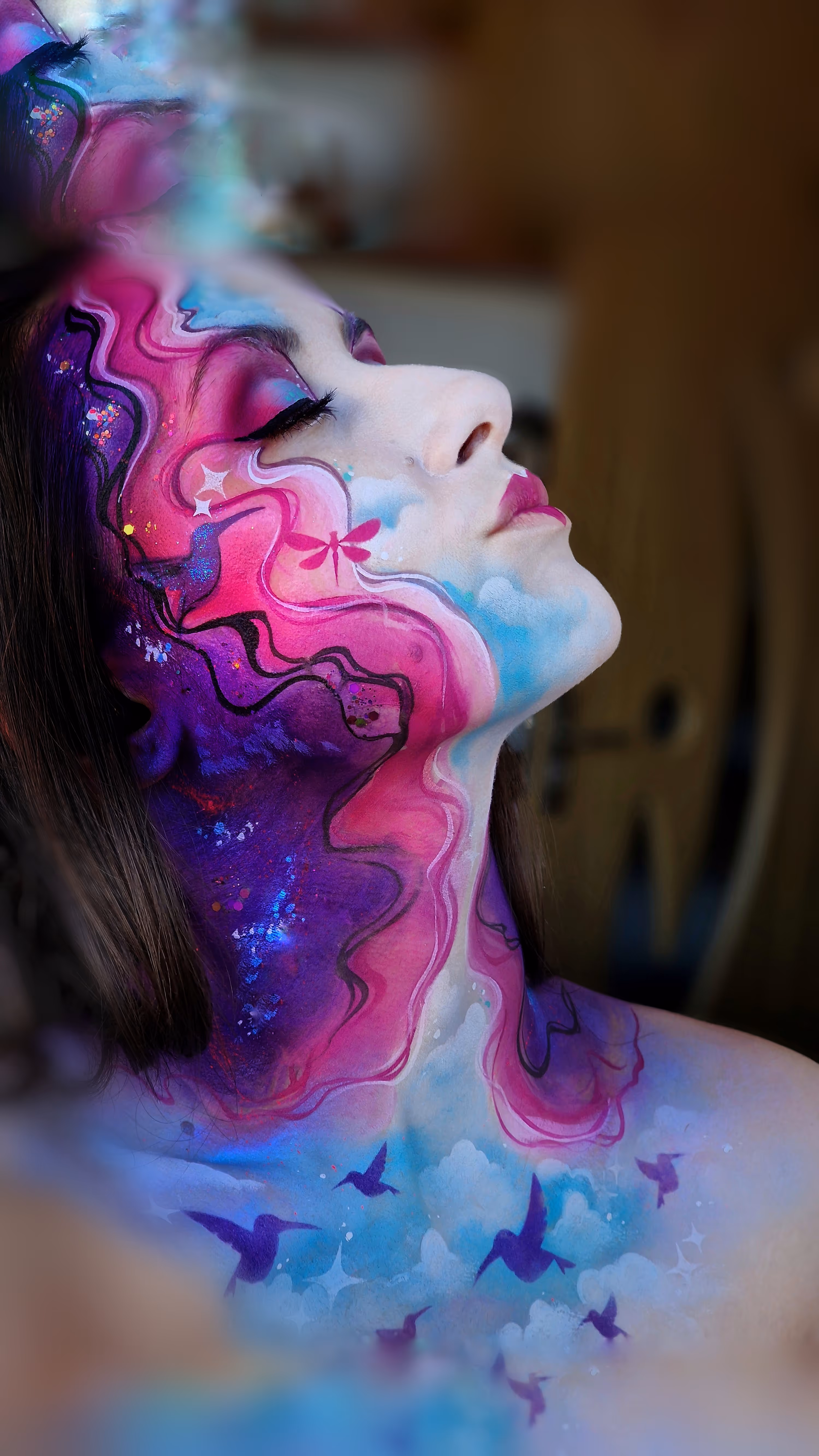 Profile of woman with face and neck painted in pink, purple, blue swirls and hummingbird designs.