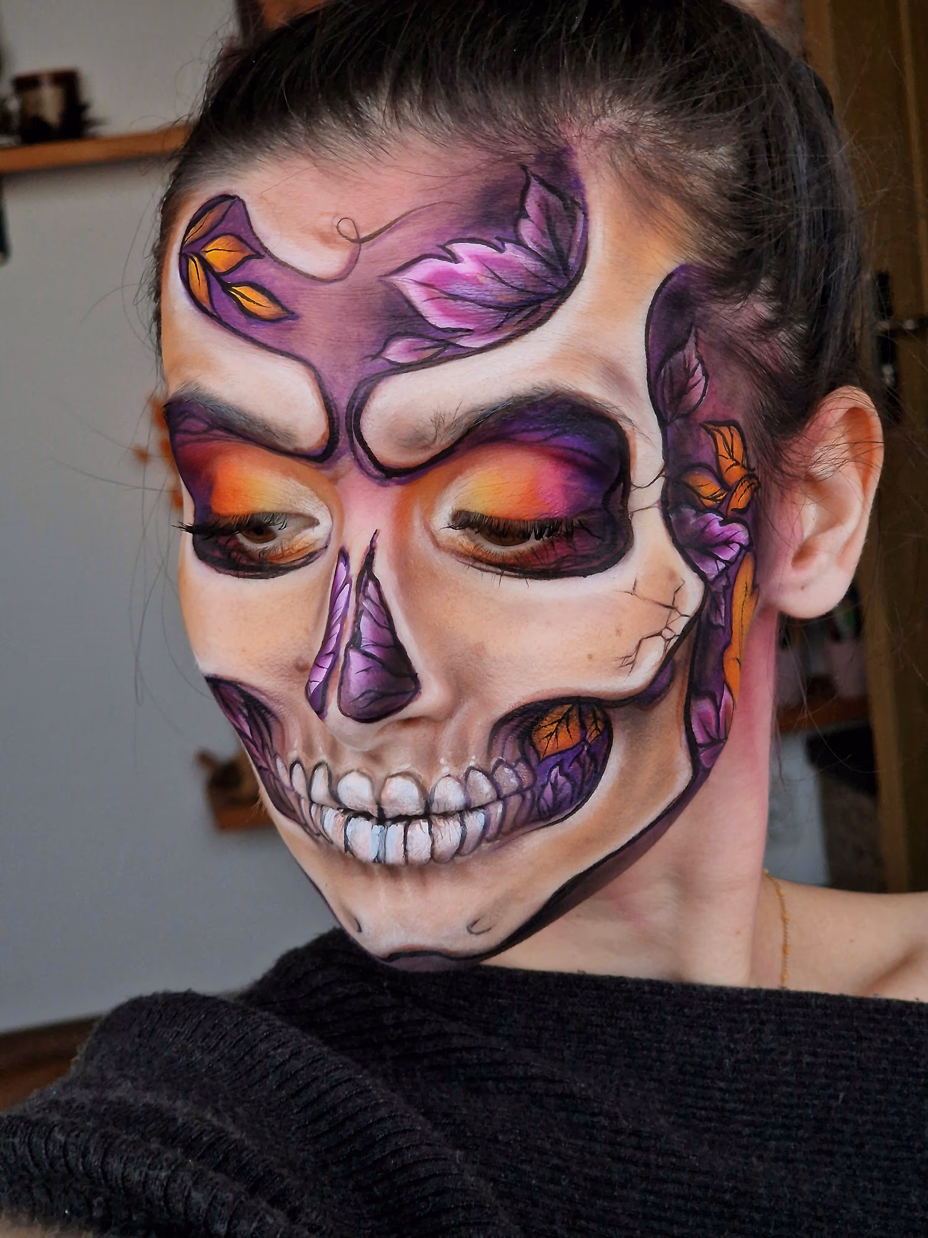 Person with detailed skull face paint featuring purple, orange, and white leaves and teeth designs.