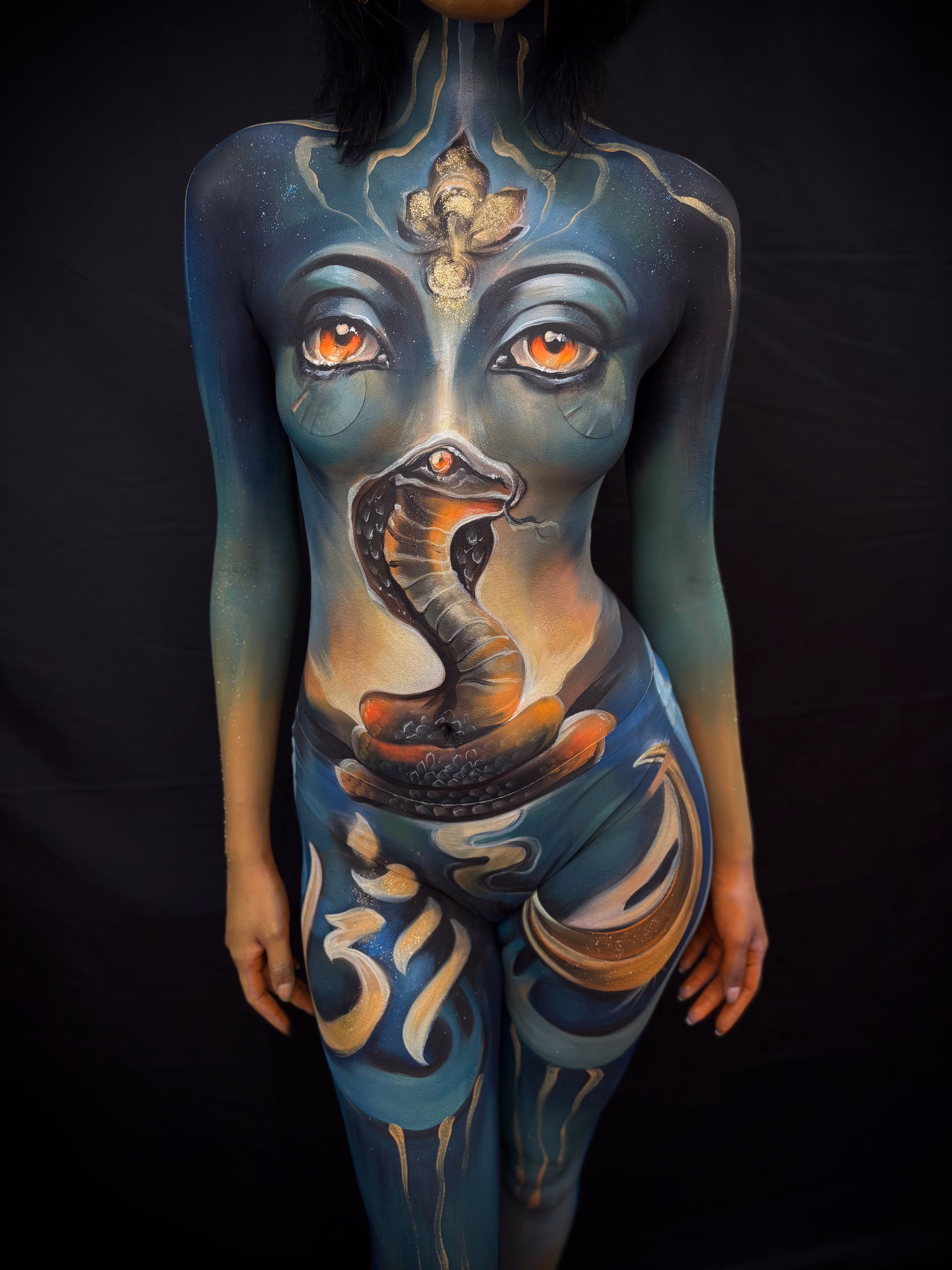 Body painting of a snake with bright eyes and artistic designs on a person's torso and legs.