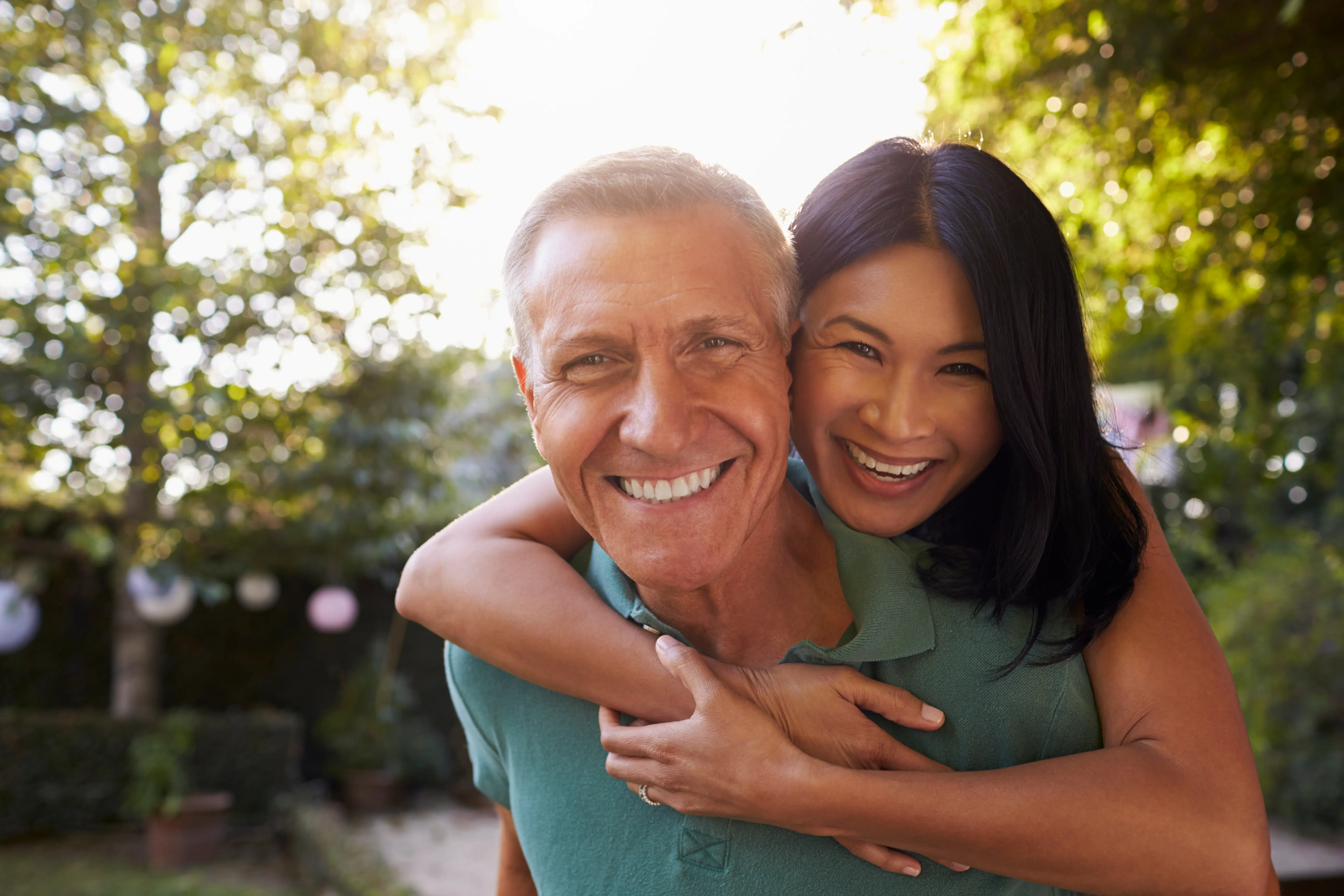 Smiling middle-aged man giving a piggyback ride to a happy woman in a green garden.
