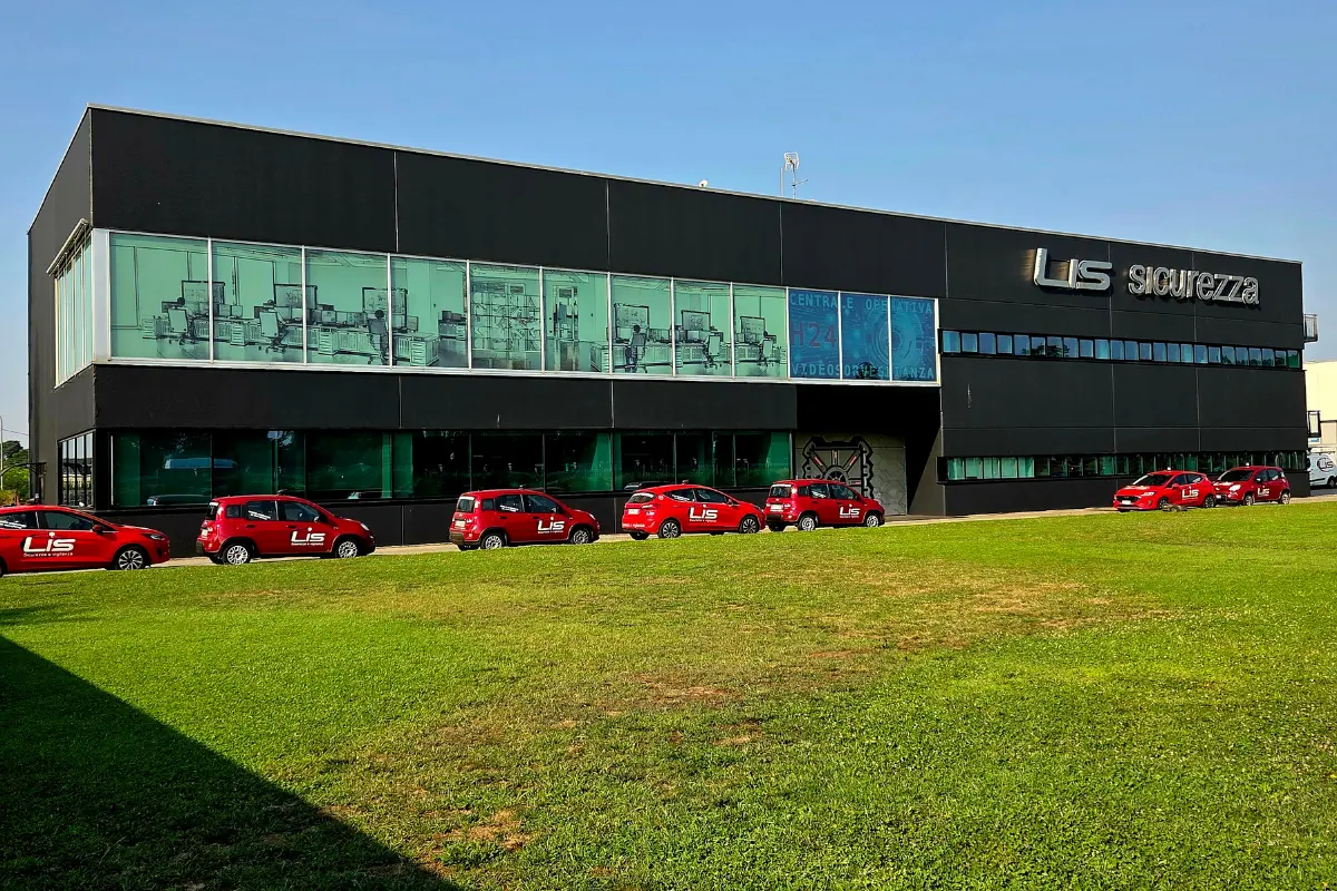 Edificio moderno nero con grande insegna Lis sicurezza e una fila di auto rosse parcheggiate davanti su un prato verde.
