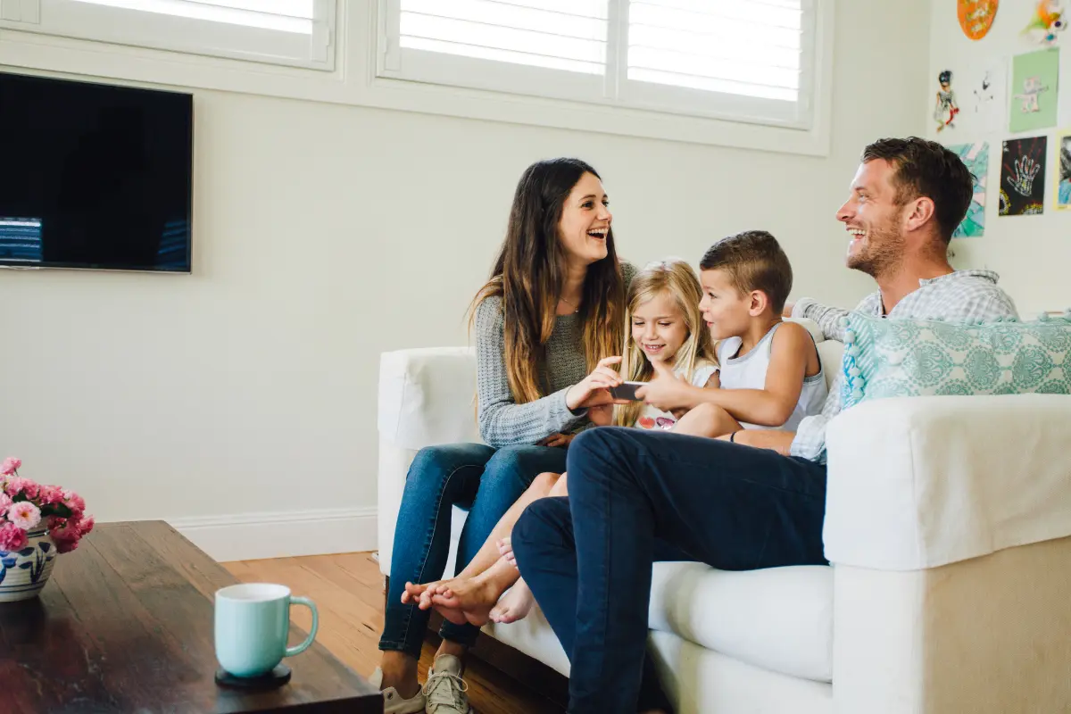 Famiglia sorridente seduta su un divano bianco con madre, padre e due bambini che interagiscono insieme.