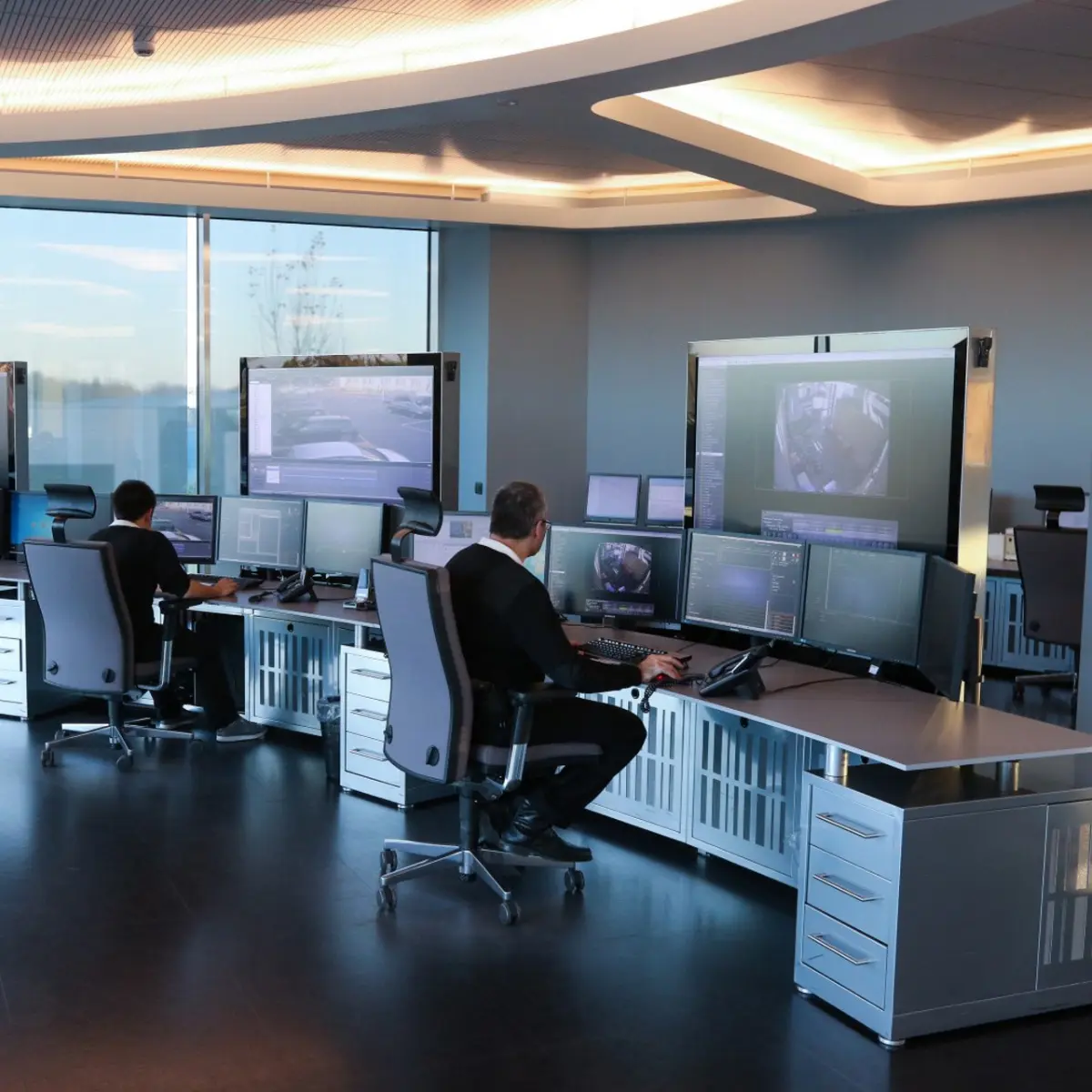 Due operatori controllano diverse immagini di video sorveglianza su più monitor in una moderna sala di controllo.