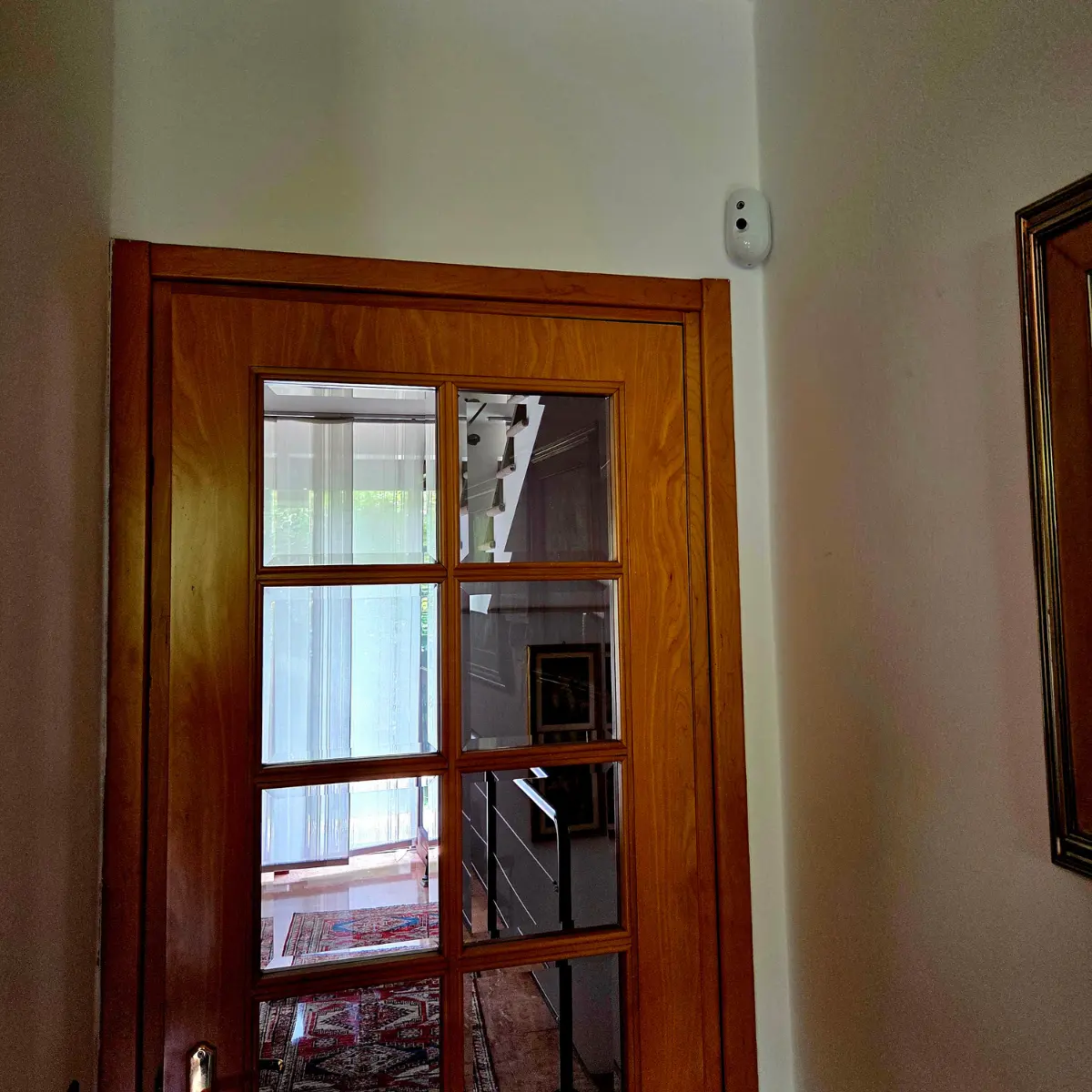 Porta in legno con vetri che riflettono una scala interna e una stanza con finestre luminose.