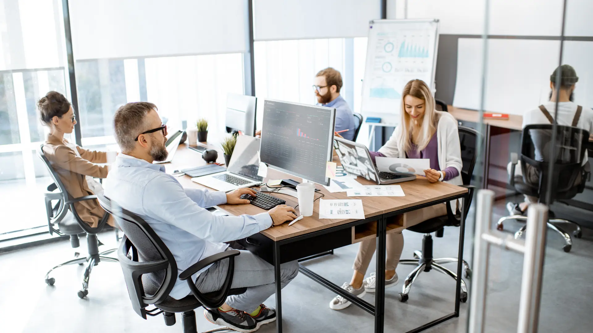 Persone al lavoro in un ufficio moderno con computer e documenti su una scrivania condivisa.