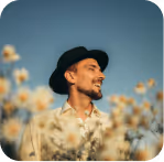 Man wearing a black hat and beige shirt smiling and looking to the side, surrounded by blurred yellow flowers under a clear sky.