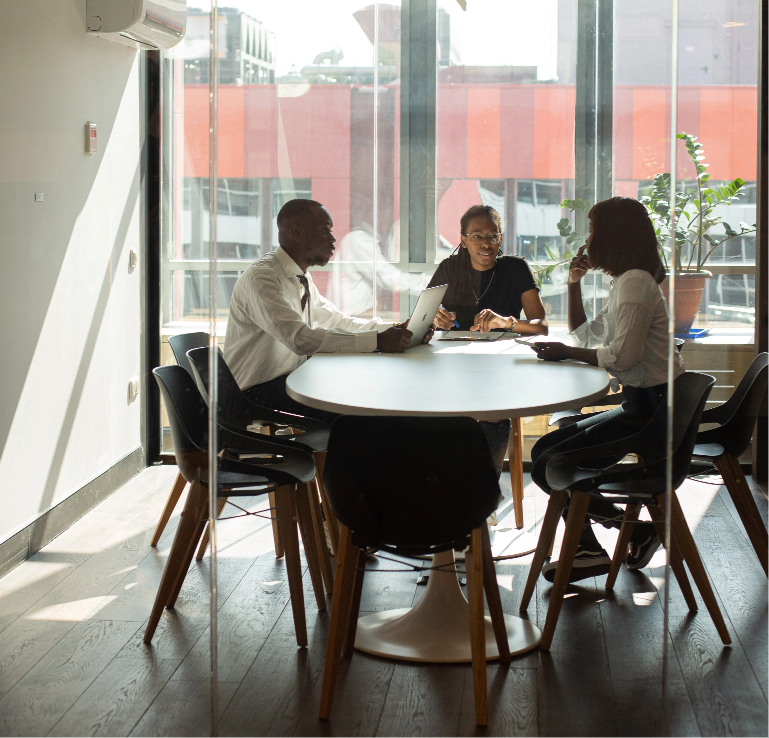 Three business professionals sitting around a table in a modern office, engaged in discussion, illustrating collaboration and consultation, featured on the FAQs page of Revenue Nomad.