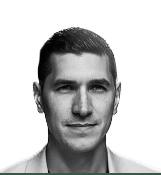 Portrait of a confident man in a light-colored blazer with short dark hair, looking forward with a neutral expression against a white background.