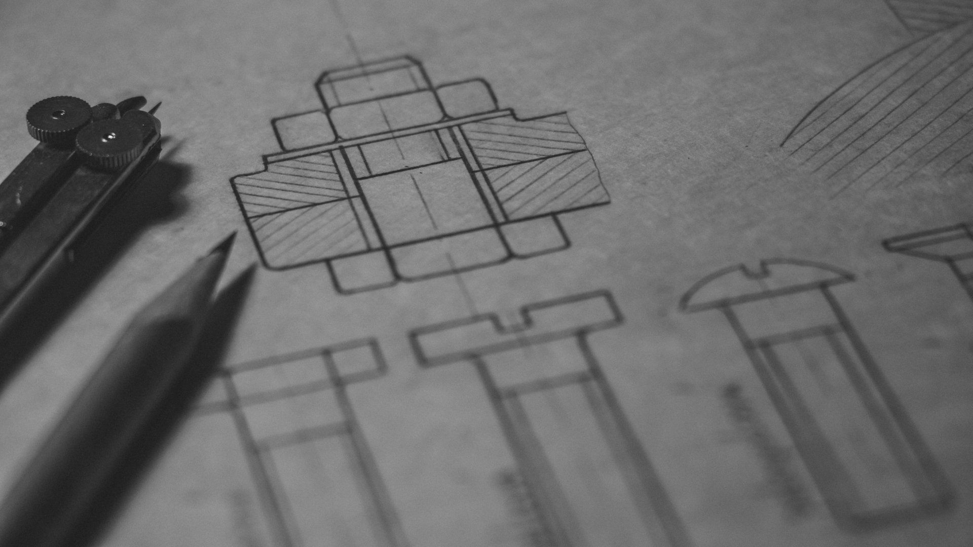 Black and white close-up of technical engineering drawings on paper, featuring detailed mechanical component schematics. A pencil and a pair of compasses rest beside the sketches, symbolizing precision and structured planning.
