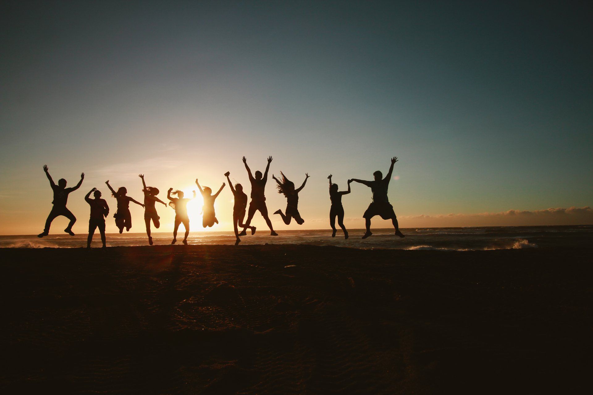 Silhouettes of a joyful team jumping on the beach at sunset, symbolizing teamwork and success.