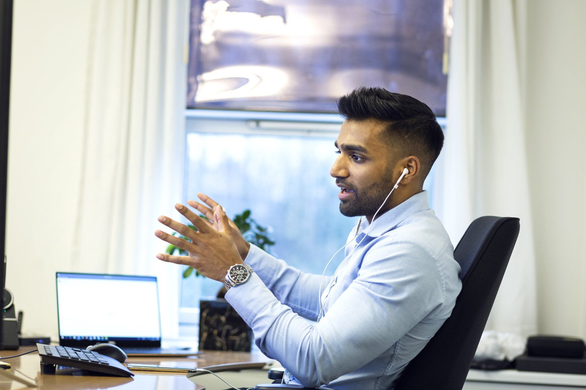 A sales executive speaking during a virtual meeting, wearing earphones and gesturing with his hands.
