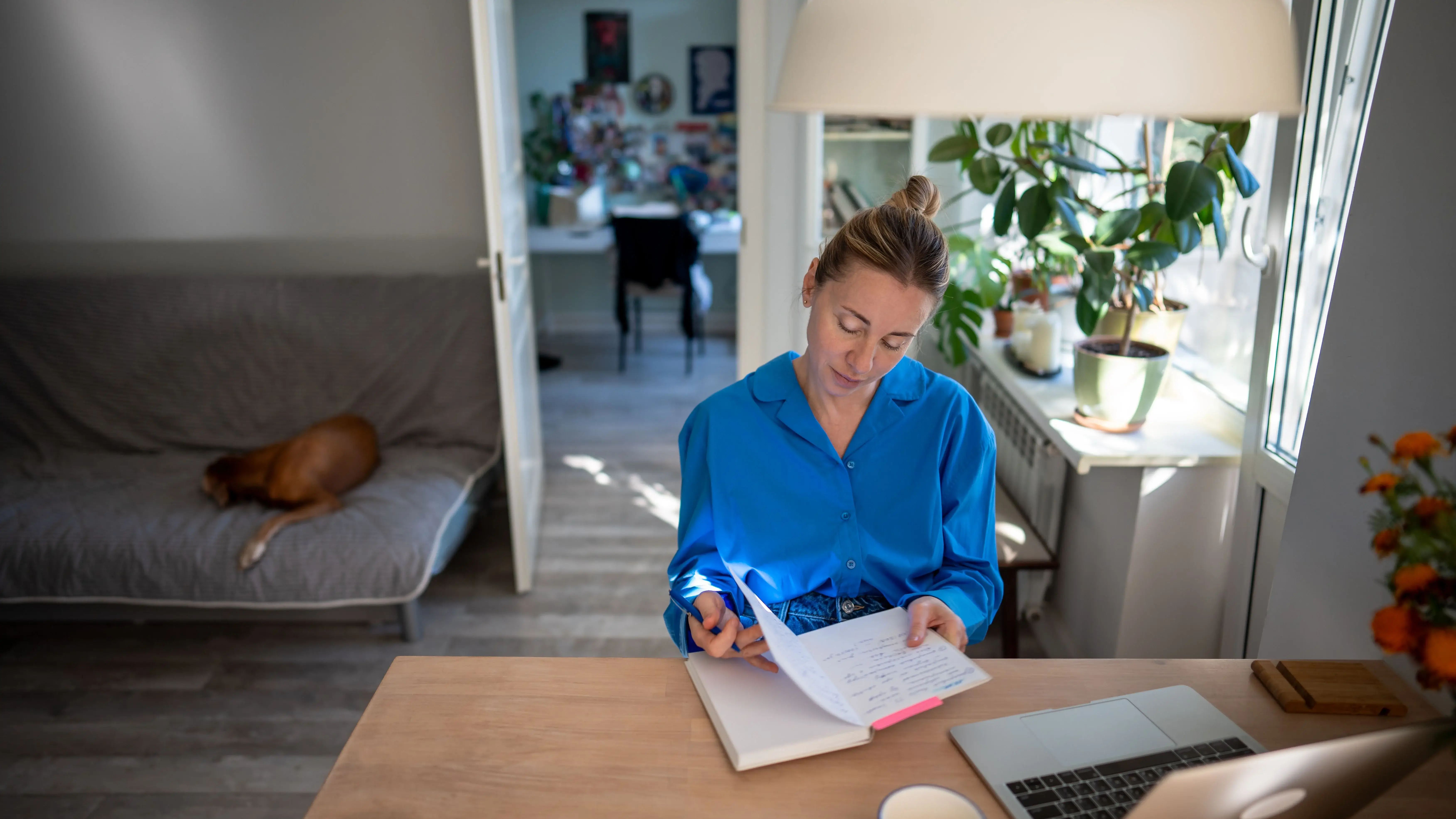 Kvinde skriver i en notesbog ved siden af sin computer.