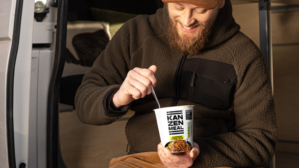 Person sits in the doorway of a camper van holding a KANZEN MEAL CUP while enjoying a meal on the go.