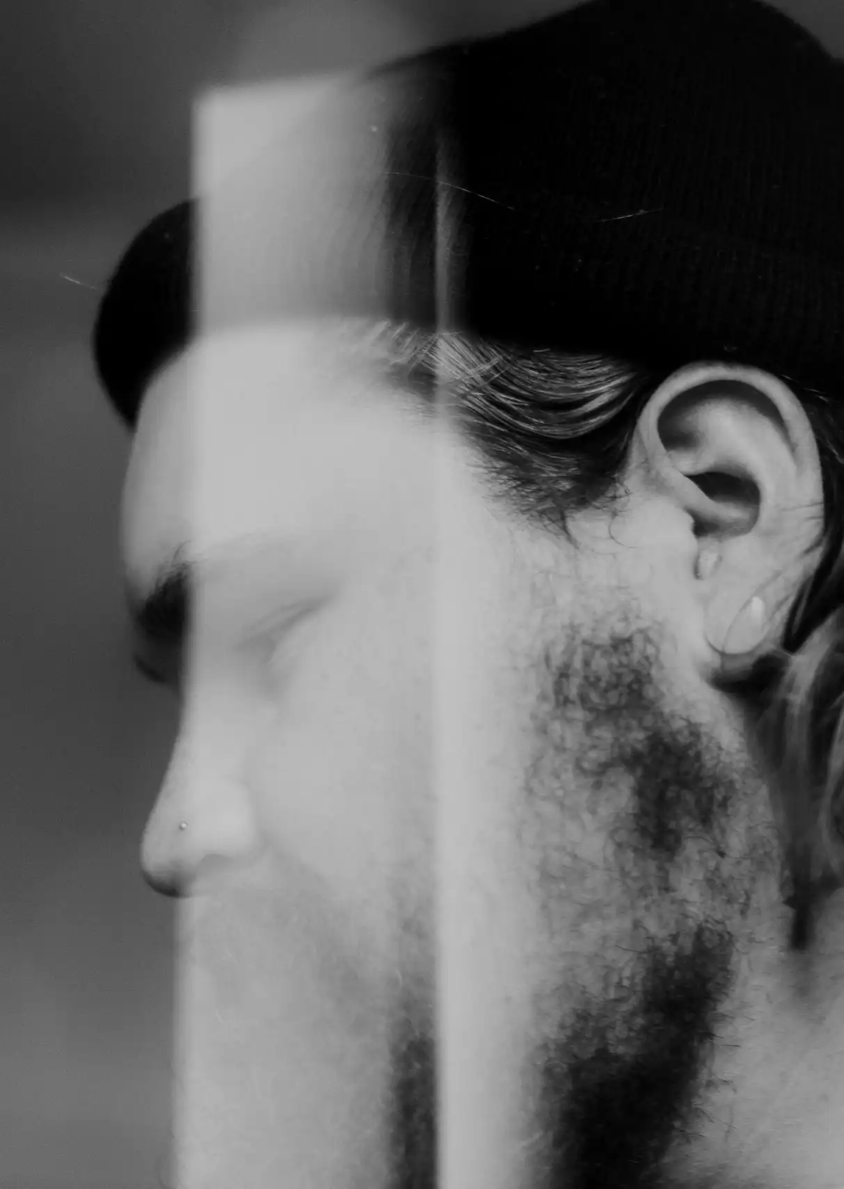 A side profile photo of a man with a beanie hat on, with glass reflection segmenting his face to symbolise stress