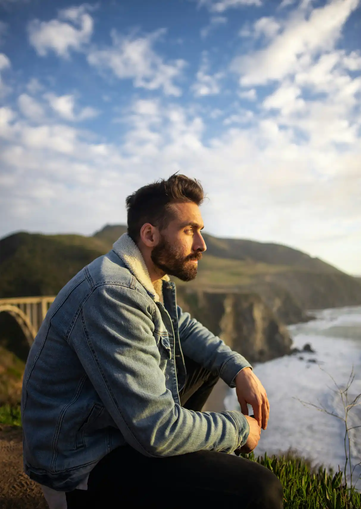 A man looks sitting near a cliff looks out over the sea