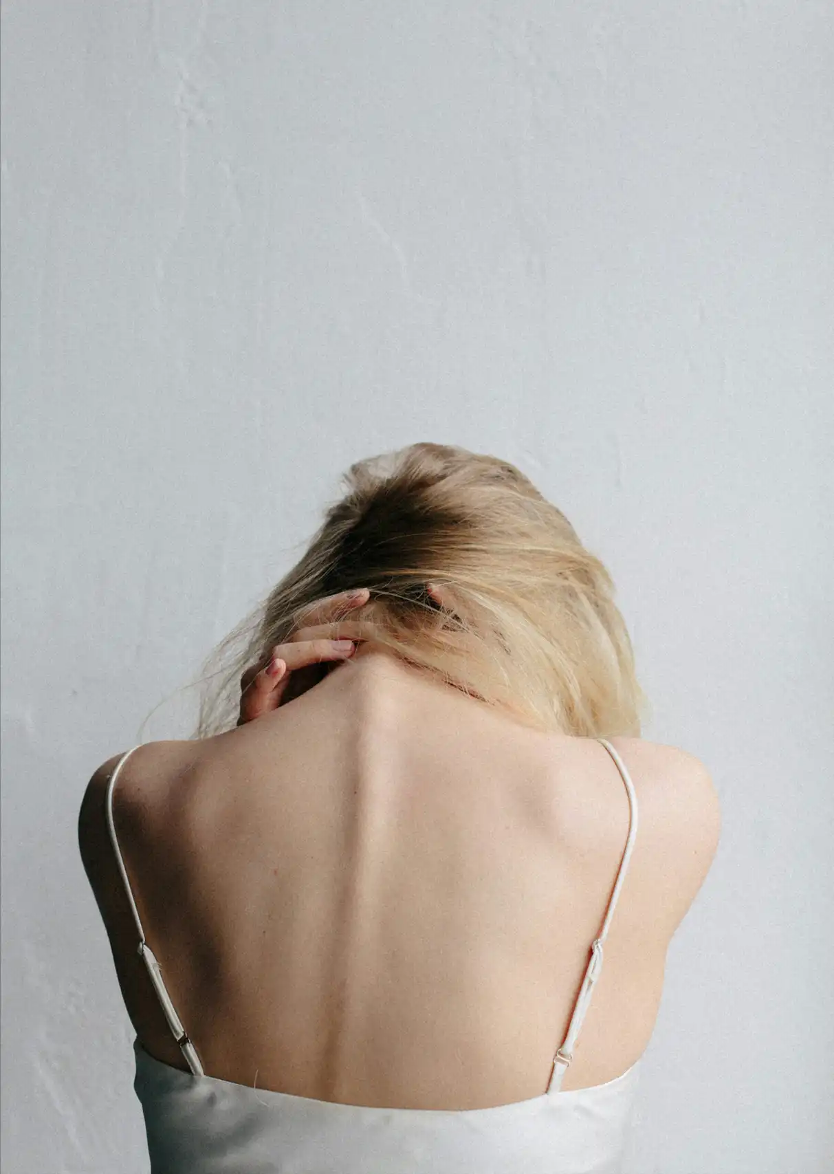 Taken from behind, a woman has her head down with her hands over her neck in pain
