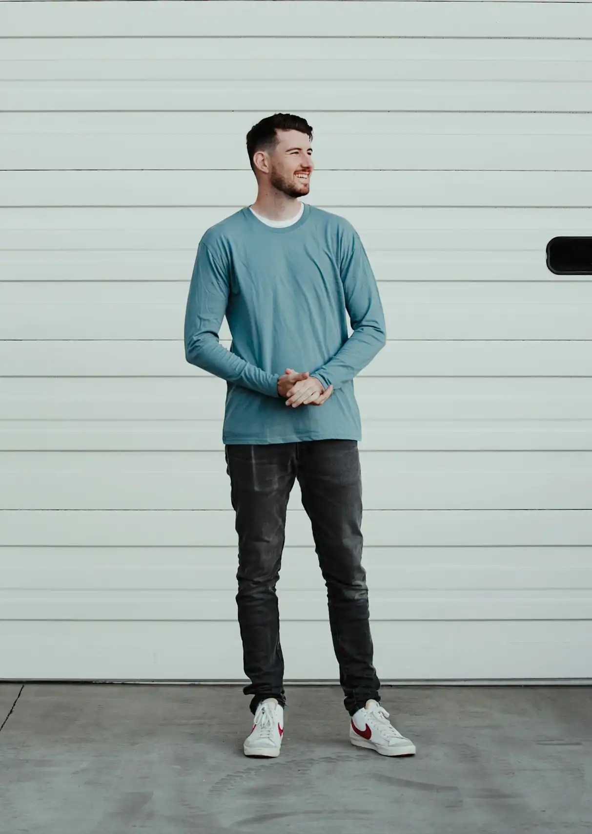 A man stood in front of a garage door with his hands together looks to his left