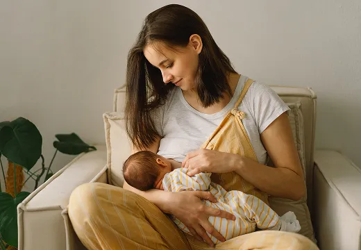 A mother holds and feeds her baby in a comfortable chair.