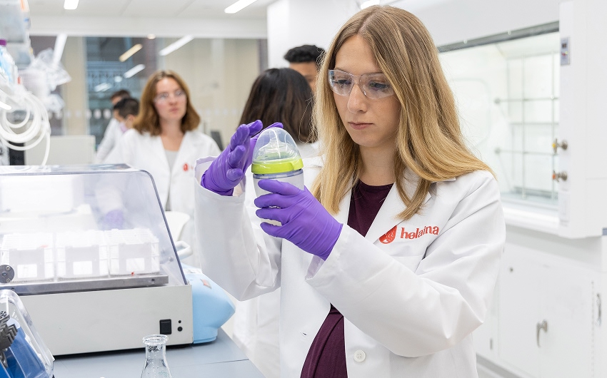Laura Katz in a lab coat and safety glasses inspects a baby bottle.