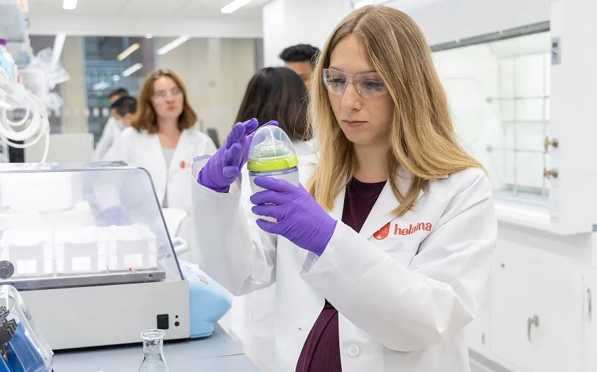 Laura Katz in a lab coat and safety glasses inspects a baby bottle.