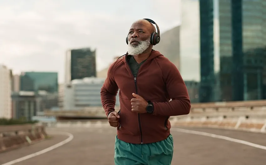 An older man with headphones runs in a city, looking determined.